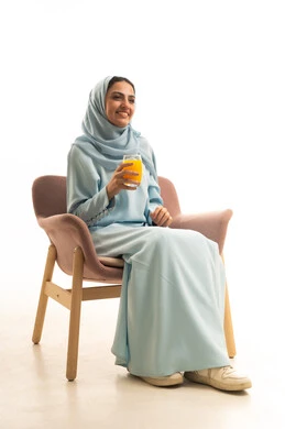 قضاء وقت ممتع و هادئ، الاستمتاع بتناول المشروبات المفيدة اللذيذة، محاولة التخفيف من حرارة الصيف بالمشروب المنعش، بورترية لإمراة عربية سعودية خليجية محجبة ترتدي العباءة تجلس على كرسي تستمع بشرب العصير الطبيعي البارد، خلفية بيضاء