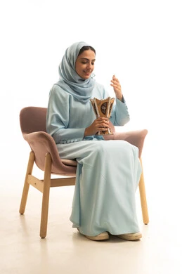 أصالة العادات و التقاليد الخليجية، مفهوم التطيب باستخدام خشب العود,إيماءات السعادة و السرور, بورتريه لامرأة عربية خليجية سعودية محجبة ترتدي العباءة تجلس على كرسي تحمل بيدها المبخرة التراثية المزخرفة, التعطر من حامل البخور, خلفية بيضاء