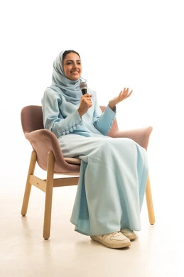 مواهب فنية في عالم الموسيقى، أداء العروض المسرحية، الفن المسرحي الغنائي، ممارسة هواية الغناء للتسلية والترفيه، بورترية لامراه عربيه خليجيه سعودية ترتدي العباءة و الحجاب  تجلس على كرسي تحمل بيديها الميكروفون، خلفية بيضاء