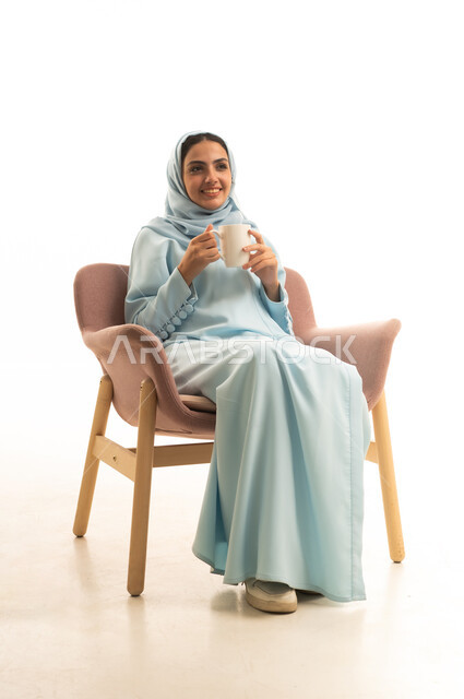 Enjoying a delicious hot drink, a portrait of a Saudi Arabian Gulf woman wearing a hijab and an abaya sitting on a chair drinking a cup of tea, expressions of happiness and joy, spending a pleasant and quiet time, white background.