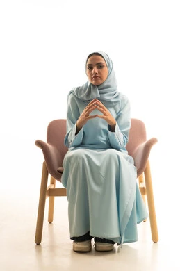 أزياء محجبات عصرية راقية، مفهوم الأناقة والاهتمام بالمظهر الخارجي، بورتريه لامرأة عربية خليجية سعودية تجلس على كرسي و تنظر الى الكاميرا بإيماءات الثقة بالنفس، خلفية بيضاء