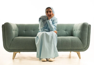 ايماءات وتعابير وجه ويدين تدل على الملل واللامبالاة، بورتريه لإمرأة عربية خليجية سعودية  تجلس على الاريكة تضع يدها على ذقنها، انتظار المواعيد، علامات حركات الملل واللامبالاة، خلفية بيضاء