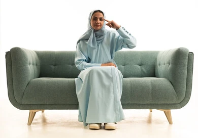 Thinking, confusion, and difficulty in choosing something, finding a solution to a specific problem, daydreaming and planning for something specific, a portrait of a Gulf Arab Saudi woman wearing an abaya sitting on a sofa with a questioning expression, a Saudi woman with her hands on her face, white background.