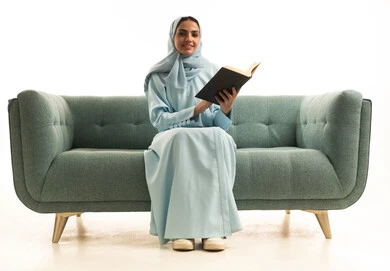 تنمية المعرفة والثقافة من خلال قراءة الكتب، ممارسة هواية المطالعة, مفهوم الشغف بالقراءة, بورتريه لامراة عربية خليجية سعودية محجبة ترتدي العباءة تجلس على  الاريكة تقوم بقراءه كتاب, كتب وروايات هادفه ومسليه، خلفيه بيضاء