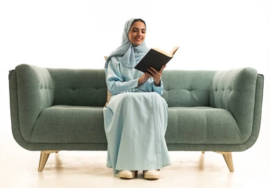 اكتساب المعرفة والتثقيف عبر قراءة الكتب، ممارسة هواية المطالعة, مفهوم الشغف بالقراءة, بورتريه لامراة عربية خليجية سعودية محجبة ترتدي العباءة تجلس على  الاريكة تقوم بقراءه كتاب, كتب وروايات هادفه ومسليه، خلفيه بيضاء