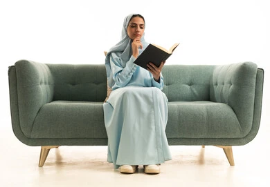 ممارسة هواية المطالعة, مفهوم الشغف بالقراءة, بورتريه لامراة عربية خليجية سعودية محجبة ترتدي العباءة تجلس على  الاريكة تقوم بقراءه كتاب, كتب وروايات هادفه ومسليه ، التعلم والتثقيف من خلال قراءه الكتب الهادفه، خلفيه بيضاء