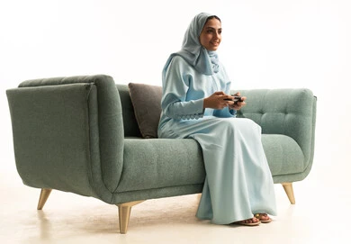 Modern electronic technologies, the concept of immersion and interaction in entertainment PlayStation games, a portrait of a Saudi Arabian Gulf woman sitting on the couch holding a game controller, enjoying a pleasant vacation, white background.