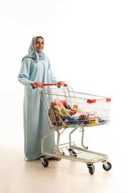 شراء المستلزمات والحاجيات الضرورية، الاستمتاع بالتجول في المول والمركز التجاري، الاستفادة من الخصومات على المنتجات، بورتريه لامرأة عربية خليجية سعودية ترتدي الحجاب والعباءة تجر عربة التسوق أمامها، الجسم بالطول الكامل، خلفية بيضاء