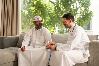 الرعاية الطبية وإجراء الفحوصات السريعة، جهاز قياس سكر الدم لمرضى السكري، العمل في القطاع الطبي وشركات التمريض المنزلي, ممرض يرتدي المعطف الطبي يقوم بفحص نسبة السكر في الدم لمريض مسن عربي خليجي سعودي يرتدي الثوب التقليدي و القبعة يجلس على الكنبه