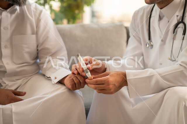 توفير خدمات الرعاية الصحية والفحص الطبي السريع، جهاز قياس سكر الدم لمرضى السكري، العمل في القطاع الطبي وشركات التمريض المنزلي,  صورة مقربة لممرض يرتدي المعطف الطبي يقوم بفحص نسبة السكر في الدم لمريض مسن عربي خليجي سعودي يرتدي الثوب التقليدي و القبعة يجلس على الكنبه