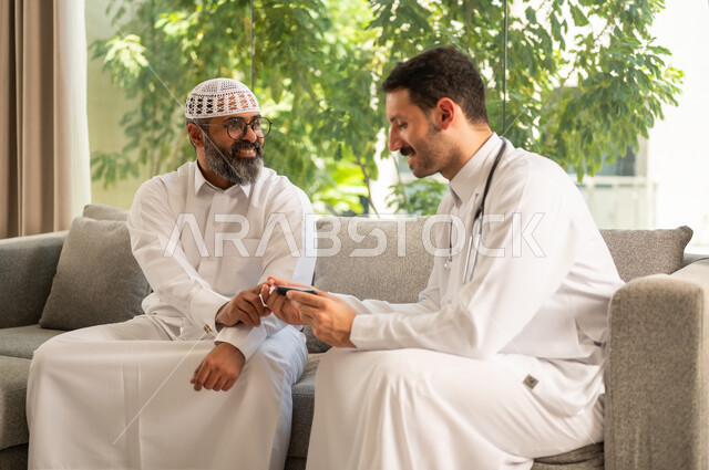جهاز قياس سكر الدم لمرضى السكري، العمل في القطاع الطبي وشركات التمريض المنزلي، الرعاية الصحية والفحص الطبي السريع, ممرض يرتدي المعطف الطبي يقوم بفحص نسبة السكر في الدم لمريض مسن عربي خليجي سعودي يرتدي الثوب و القبعة البيضاء يجلس على الكنبه