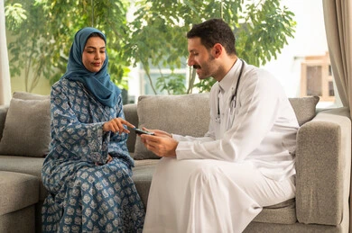 العناية الطبية المتواصلة بمرضى السكري, الفحوصات الطبية السريعة لمعرفة نسبة السكر في الدم، استخدام الأجهزة الالكترونية للتحاليل المنزلية، شابة سعودية مصابة بحالة مرضية مزمنة, طبيب عربي خليجي سعودي يرتدي المعطف الطبي يقوم بوخز اصبع امرأة