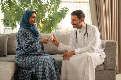 الاطمئنان الدوري على صحة مرضى السكري, الفحوصات الطبية السريعة لمعرفة نسبة السكر في الدم، استخدام الأجهزة الالكترونية للتحاليل المنزلية، شابة سعودية مصابة بحالة مرضية مزمنة, طبيب عربي خليجي سعودي يرتدي المعطف الطبي يقوم بوخز اصبع امرأة