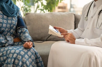 Healthcare and rapid medical examination, a close-up image of a Saudi Arabian Gulf Arab doctor wearing a medical coat measuring the patient's blood pressure at home, using a modern and advanced electronic scale for home examination.