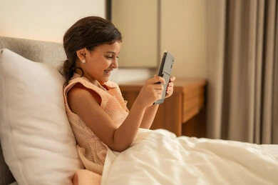 The use of a modern and advanced technical device, following lessons remotely via the internet, the concept of e-learning, educational scientific curricula, an Arab Gulf Saudi girl wearing a dress sitting on the bed holding a tablet in her hand.