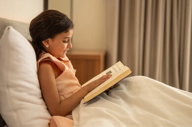 إيماءات الانتباه والتركيز بالمطالعة, الاهتمام بتصفح الكتب المفيدة, تنمية مهارات القراءة للأطفال, تمضية أوقات الفراغ بالتعلم والتثقف الذاتي, فتاة عربية خليجية سعودية تجلس على السرير تقوم بالقراءة بتمعن, مطالعة القصص التصويرية المسلية