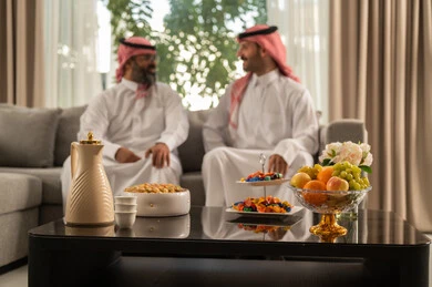 الاستمتاع بقضاء وقت مع الابناء، جلسة عائلية سعيدة، التسامر وتبادل الاحاديث، تعابير المودة والمحبة، رجل كبير بالسن عربي خليجي سعودي يرتدي الثوب التقليدي والشماغ يجلس على الاريكة برفقة ابنه، ايماءات السعادة و السرور