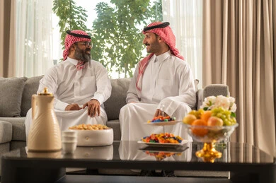 جلسة عائلية سعيدة، التسامر وتبادل الاحاديث، تعابير المودة والمحبة، الاستمتاع بقضاء وقت مع الابناء، رجل كبير بالسن عربي خليجي سعودي يرتدي الثوب التقليدي والشماغ يجلس على الاريكة برفقة ابنه، ايماءات السعادة و السرور