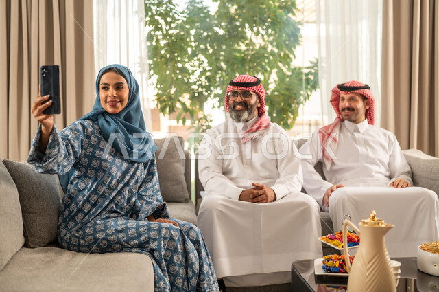 أخذ صورة سيلفي عبر الهاتف المحمول، ضيافة وحلوى العيد، حسن استقبال وإكرام الضيف، فرحة وبهجة الابناء في ايام العيد السعيد, التجمعات والزيارات الاسرية في الأعياد والمناسبات الاسلامية, رجل عربي خليجي سعودي يرتدي الثوب التقليدي يجلس مع أحفاده بإيماءات الفرح والسرور