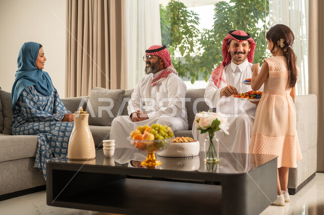 ضيافة العيد مع الحلوى، مناقشات و حوارات اسرية ، فرحة وبهجة الابناء في ايام العيد السعيد, التجمعات والزيارات الاسرية في الأعياد والمناسبات الاسلامية, رجل عربي خليجي سعودي يرتدي الثوب التقليدي يجلس مع أحفاده بإيماءات الفرح والسرور، صلة الرحم والترابط الاسري