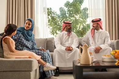 Honoring the guest and welcoming them warmly, maintaining family ties and connections, the joy and happiness of children during the blessed Eid days, family gatherings and visits during Islamic holidays and occasions, an Arab Gulf Saudi man wearing traditional attire sitting with his grandchildren with gestures of joy and happiness, hospitality and Eid sweets.