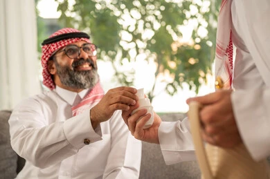 A family gathering during holidays and occasions, hospitality and reception, a Saudi Arabian Gulf man wearing traditional attire and a ghutrah serving hot coffee, the joy and happiness of Eid among family and relatives, Eid traditions in Saudi Gulf society, the atmosphere of the Saudi family during Eid.