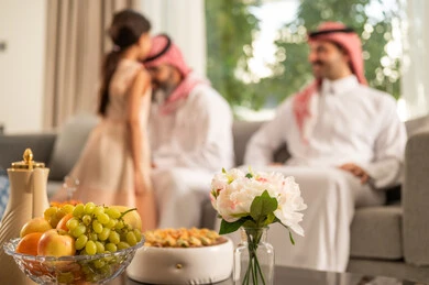 رجل عربي خليجي سعودي يرتدي الثوب التقليدي يجلس مع أحفاده بإيماءات الفرح والسرور، التجمعات والزيارات الاسرية في الأعياد والمناسبات الاسلامية، فرحة وبهجة الابناء في ايام العيد السعيد، ضيافة وحلوى العيد، حسن استقبال وإكرام الضيف، صلة الرحم والترابط الاسري، طفلة عربيه خليجيه سعودية ترتدي الفستان تقوم بتقبيل رأس جدها