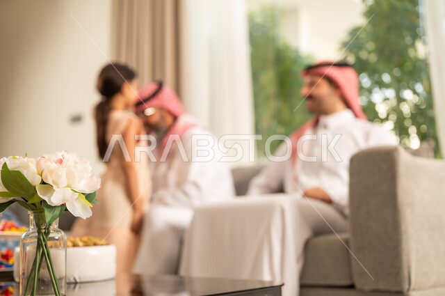 The joy and happiness of children during the blessed Eid days, family gatherings and visits during Islamic holidays and occasions, an Arab Gulf Saudi man wearing traditional attire sitting with his grandchildren with gestures of joy and delight, hospitality and Eid sweets, good reception and honoring the guest, maintaining family ties and connections, an Arab Gulf Saudi girl wearing a dress kissing her grandfather's head.
