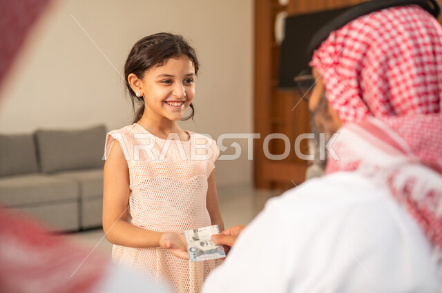جد عربي خليجي سعودي يرتدي الثوب التقليدي والشماغ  يعطي الفلوس لحفيدته،  دور الأب في حياه الأبناء، مفهوم الحب والحنان، تقديم العيدية في العيد، عادات وتقاليد الاعياد والمناسبات الدينية، ايماءات السعادة والسرور، اجواء اسرية مليئة بالفرح