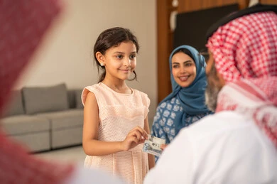 The concept of love and affection, giving Eid gifts during the holiday, the role of the father in the lives of children, a Saudi Gulf Arab grandfather wearing traditional attire and a headscarf giving money to his granddaughter, customs and traditions of holidays and religious occasions, gestures of happiness and joy, a family atmosphere filled with joy.