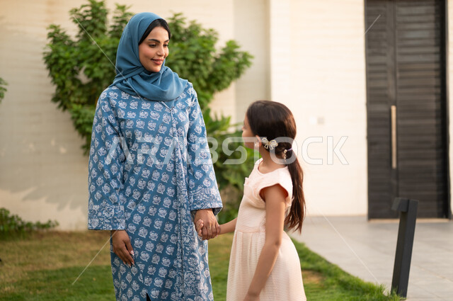 ام عربية خليجية سعودية محجبة ترتدي العباءة تنظر الى ابنتها بايماءات السعادة و السرور، شاليه ومنتجع ترفيهي في المملكة، مفهوم الترابط الأسري المبني على المحبه، الاستمتاع بالإجازة الصيفية برفقة العائلة، قضاء وقت ممتع ومنعش في فصل الصيف