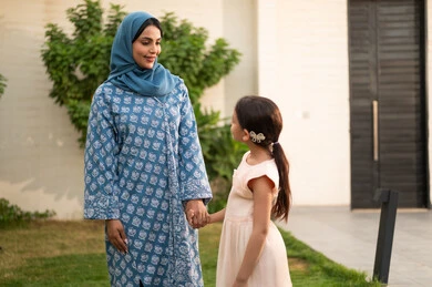 ام عربية خليجية سعودية محجبة ترتدي العباءة تنظر الى ابنتها بايماءات السعادة و السرور، شاليه ومنتجع ترفيهي في المملكة، مفهوم الترابط الأسري المبني على المحبه، الاستمتاع بالإجازة الصيفية برفقة العائلة، قضاء وقت ممتع ومنعش في فصل الصيف