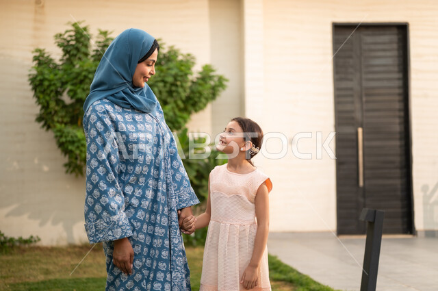 A chalet and recreational resort in the Kingdom, a concept of family bonding based on love, enjoying the summer vacation with family, spending enjoyable and refreshing time in the summer, an Arab Gulf Saudi mother wearing a hijab and an abaya looking at her daughter with gestures of happiness and joy.