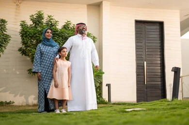 Spending quality time with children, maintaining family bonds, caring for and attending to children, playing, having fun, and enjoying leisure time with the family outdoors; a Saudi Arabian Gulf couple playing in the park with their daughter, beaming with happiness.