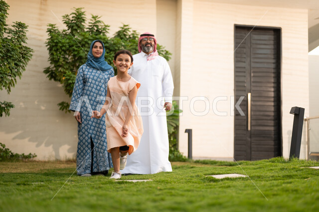 الاستمتاع بوقت جميل مع الأبناء، المحافظة على الترابط الأسري، الاعتناء والاهتمام بالاولاد, اللعب والتسلية والترفيه مع العائلة في الهواء الطلق، زوجان عربيان خليجيان سعوديان يلعبان في الحديقة مع ابنتهما بإيماءات السعادة