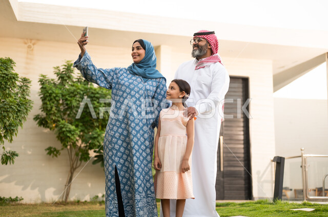 التقاط صورة سيلفي تذكارية عبر الهاتف المحمول، شاليه ومنتجع ترفيهي في المملكة، الاستمتاع بالإجازة الصيفية برفقة العائلة، ايماءات السعادة والسرور، قضاء وقت ممتع ومنعش في فصل الصيف، الأجواء العائلية المليئة بالحب، عائلة عربية خليجية سعودية مبتسمة تمشي في المنتزه