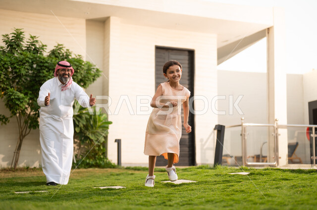 اللعب والتسلية مع العائلة في الأجواء الخارجية, قضاء أوقات ممتعه مع الأبناء، رجل عربي خليجي سعودي يرتدي الثوب التقليدي والشماغ يلعب في الحديقة مع ابنته بإيماءات السعادة، المحافظة على الترابط الأسري، الاعتناء والاهتمام بالاولاد