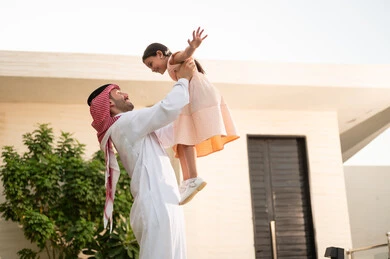 قضاء أوقات ممتعه مع الأبناء، رجل عربي خليجي سعودي يرتدي الثوب التقليدي والشماغ يرفع ابنته عاليا بإيماءات السعادة، المحافظة على الترابط الأسري، الاعتناء والاهتمام بالاولاد، اللعب والتسلية والترفيه مع العائلة في الهواء الطلق