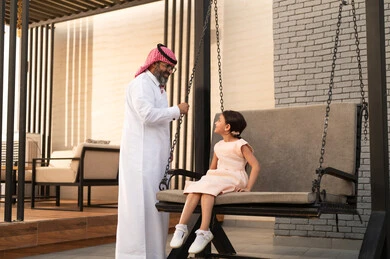 اللعب في أجواء مشمسة والاستمتاع بالوقت، فتاة عربيه سعوديه خليجيه مبتسمة تلعب في المنتزه بتعابير السرور والسعادة برفقة والدها، قضاء وقت ترفيهي في الخارج، التأرجح على الأرجوحه