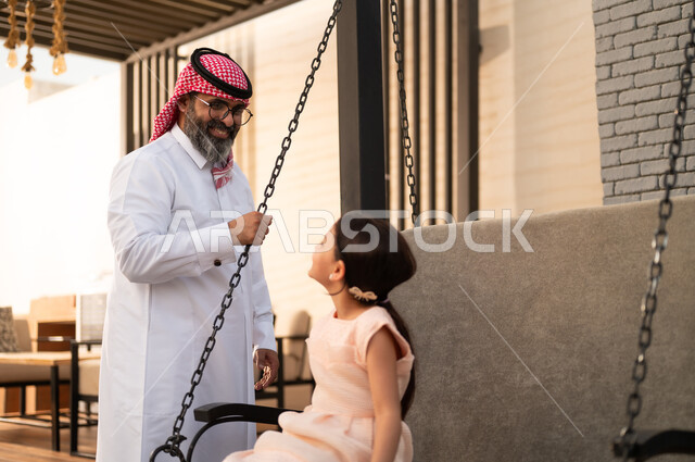 قضاء لحظات ممتعة باللعب في طقس مشمس، فتاة عربيه سعوديه خليجيه مبتسمة تلعب في المنتزه بتعابير السرور والسعادة برفقة والدها، قضاء وقت ترفيهي في الخارج، التأرجح على الأرجوحه