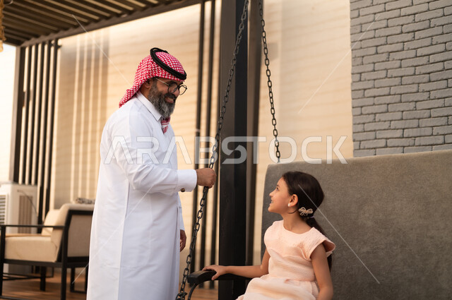 الإستمتاع باللعب في يوم مشمس، التأرجح على الأرجوحه, قضاء وقت ممتع في الخارج، فتاة عربيه سعوديه خليجيه مبتسمة تلعب في المنتزه بتعابير السرور والسعادة برفقة والدها