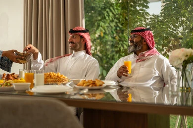 اجتماع الأسرة حول مائدة الإفطار المليئة بأصناف المأكولات والمقبلات الشهية، أجواء عائلية روحانية دينية إسلامية، كسر الصيام بالتمر عند أذان المغرب في رمضان المبارك، فطور رمضاني عائلي، صورة مقربة ليد امراه عربيه خليجيه سعودية تقوم بتقديم الطعام, حسن الضيافة وإكرام الأخرين