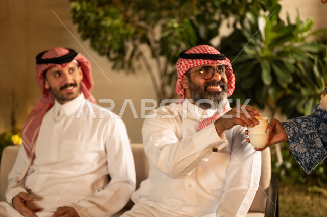 تقديم القهوة العربية في المناسبات الاسلامية,  صورة مقربة ليد امراة عربية خليجية سعودية  تقوم بتقديم فنجان القهوة, الاستمتاع بالمشروبات الساخنة, حسن الاستقبال واكرام الضيف، صلة الرحم والترابط الاسري، التجمعات والزيارات الاسرية في الأعياد والمناسبات الاسلامية
