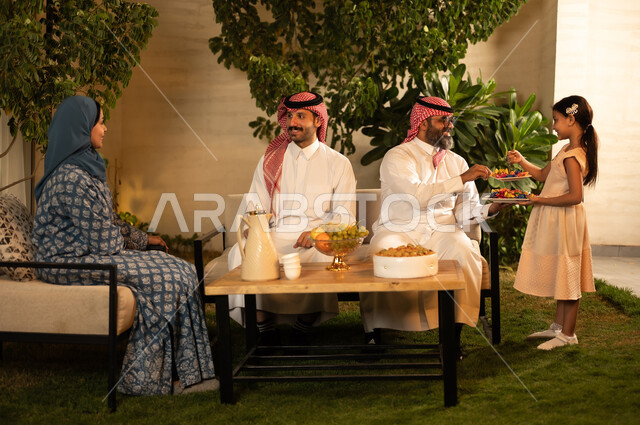 بهجة وفرحة العيد المبارك, أجواء المجتمع السعودي في المناسبات والأعياد السعيدة, العادات والتقاليد والقيام بالزيارات العائلية, مفهوم اكرام الضيف وحسن الاستقبال، ضيافة و حلوي العيد،  رجل عربي خليجي سعودي يرتدي الثوب التقليدي يجلس مع أحفاده بإيماءات الفرح والسرور