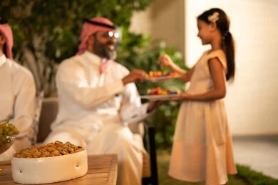 الاجتماعات العائلية في الأعياد والمناسبات الإسلامية، حسن استقبال وإكرام الضيف، صلة الرحم والترابط الاسري, فرحة وبهجة الابناء في ايام العيد السعيد, رجل عربي خليجي سعودي يرتدي الثوب التقليدي يجلس مع أحفاده بإيماءات الفرح والسرور، ضيافة وحلوى العيد