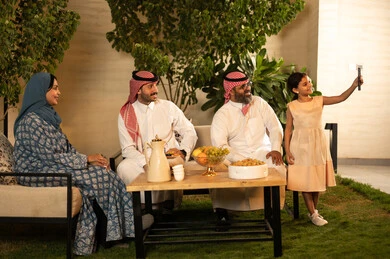 التقاط صورة سيلفي عبر الهاتف المحمول، ضيافة وحلوى العيد، حسن استقبال وإكرام الضيف، فرحة وبهجة الابناء في ايام العيد السعيد, التجمعات والزيارات الاسرية في الأعياد والمناسبات الاسلامية, رجل عربي خليجي سعودي يرتدي الثوب التقليدي يجلس مع أحفاده بإيماءات الفرح والسرور