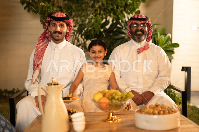 النظر للكاميرا بتعابير السرور، صلة الرحم والترابط الاسري, التجمعات والزيارات الاسرية في الأعياد والمناسبات الاسلامية, رجل عربي خليجي سعودي يرتدي الزي التقليدي يجلس مع أحفاده ، ضيافة وحلوى العيد، حسن استقبال وإكرام الضيف