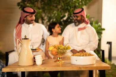 صلة الرحم والترابط الاسري, فرحة وبهجة الابناء في ايام العيد السعيد, التجمعات والزيارات الاسرية في الأعياد والمناسبات الاسلامية, رجل عربي خليجي سعودي يرتدي الزي التقليدي يجلس مع أحفاده بإيماءات الفرح والسرور، ضيافة وحلوى العيد، حسن استقبال وإكرام الضيف