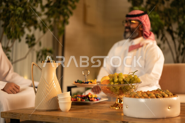ايماءات السعادة و السرور، تقديم الضيافة العربية مع الفاكهة والقهوة، مفهوم الضيافة والتواصل الاجتماعي, رجلان عربيان خليجيان سعوديان يرتديان الثوب والشماغ يقومان بتبادل الحديث في أجواء ودية