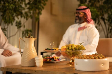 ايماءات السعادة و السرور، تقديم الضيافة العربية مع الفاكهة والقهوة، مفهوم الضيافة والتواصل الاجتماعي, رجلان عربيان خليجيان سعوديان يرتديان الثوب والشماغ يقومان بتبادل الحديث في أجواء ودية